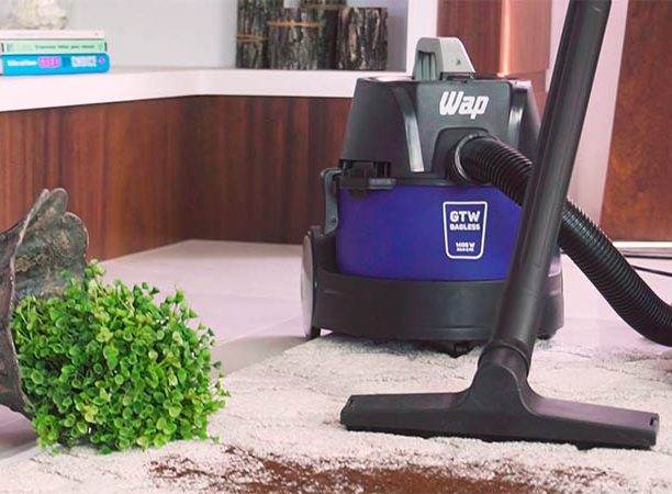 A imagem mostra um aspirador de pó sendo utilizado para limpar um carpete sujo de terra. É uma limpeza à seco